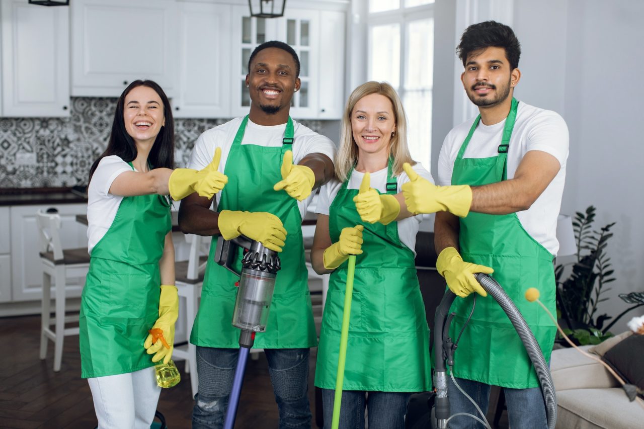 smiling multiracial team of professional cleaners showing thumbs up to camera